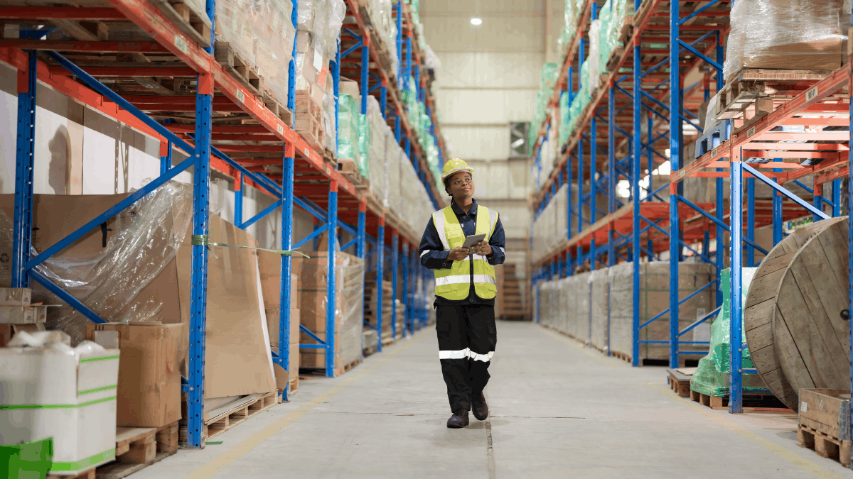 Warehouse supervisor walking a racked aisle with a tablet